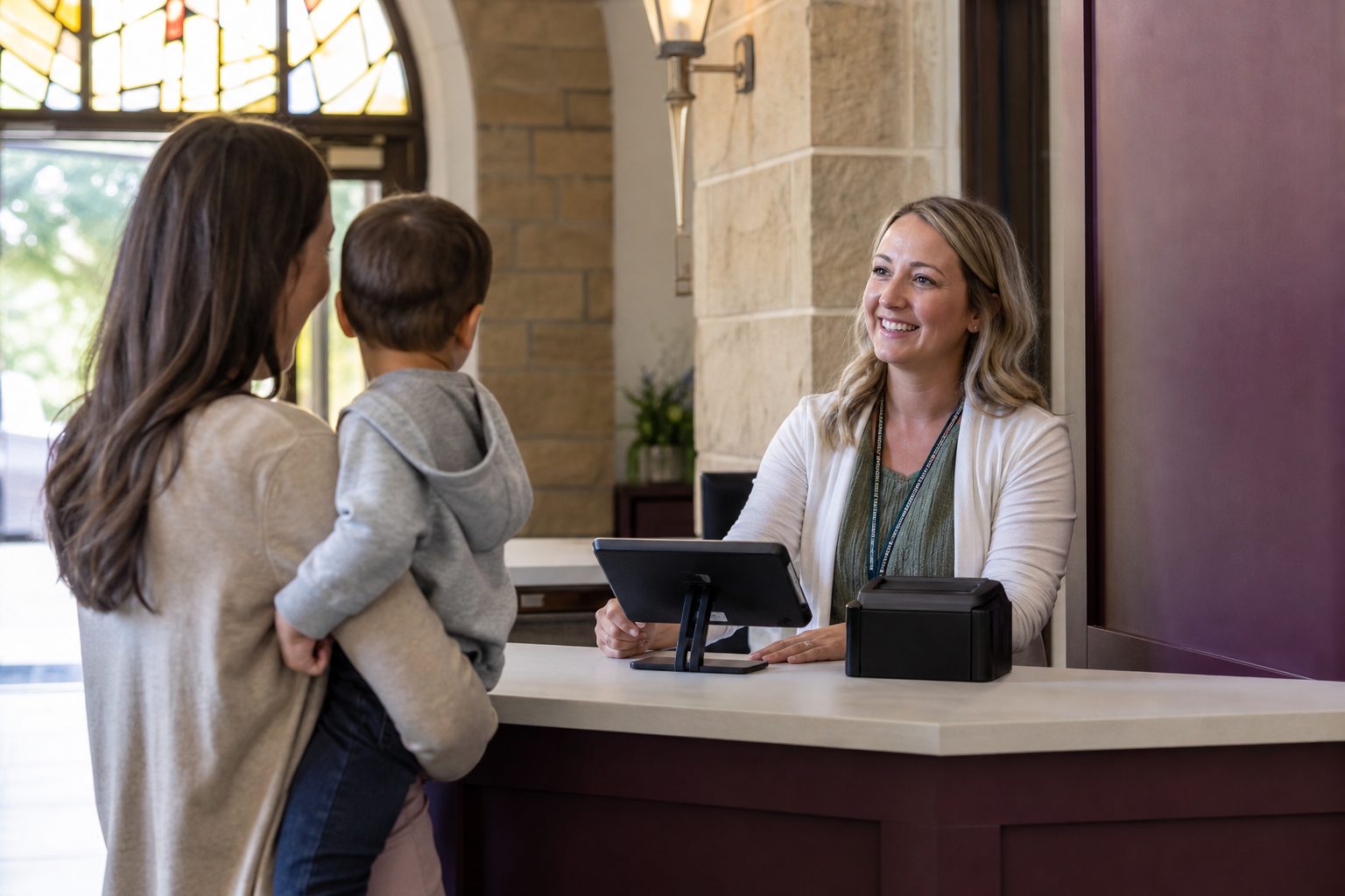Volunteer standing at a children's check in counter with a tablet and label printer in a sunlit church lobby.